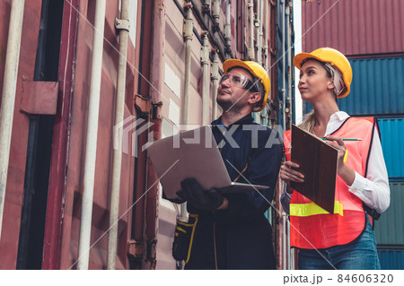 Industrial worker works with co-worker at overseas shipping container yard Industrial worker works with co-worker at overseas shipping container yard 84606320