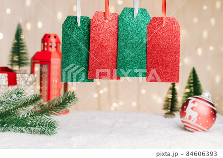 Four Gift tags or labels with copy space for text on festive Christmas composition with fir tree branch, red ball decor, lantern on the snow against a warm lights bokeh background. Selective focus. Four Gift tags or labels with copy space for text on festive Christmas composition with fir tree branch, red ball decor, lantern on the snow against a warm lights bokeh background. Selective focus. 84606393