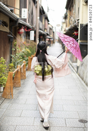 京都府京都市東山区の町を和傘を持って歩く着物姿の若い女性の後ろ姿の写真素材