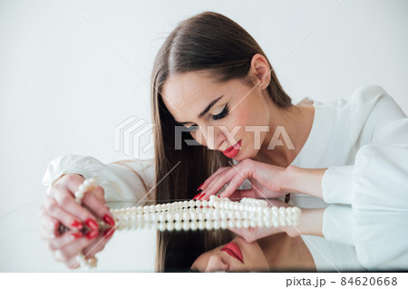 portrait of a beautiful brunette woman at the mirror with pearl beads portrait of a beautiful brunette woman at the mirror with pearl beads 84620668