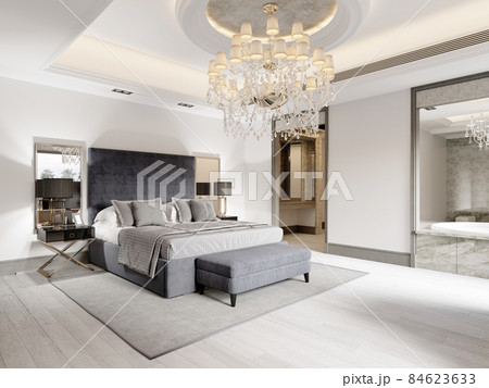 Luxurious bedroom with white walls and a gray fabric bed with black bedside tables and lamps and a large luminous crystal chandelier. 84623633