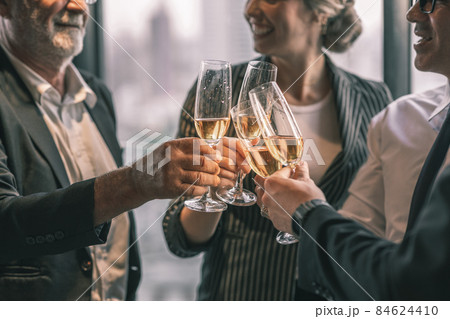 Picture of young business man and woman talking to his older business partner. They are in white shirt and black tie. They are sitting on a table in a hotel lobby. They are holding a champagne glass. Picture of young business man and woman talking to his older business partner. They are in white shirt and black tie. They are sitting on a table in a hotel lobby. They are holding a champagne glass. 84624410