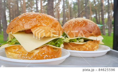 Close-up of two large DIY hamburgers in the park on a barbecue, rest and cooking on a picnic in the summer, food, delicious, bright colors. Unhealthy food concept. Fast food. Close-up of two large DIY hamburgers in the park on a barbecue, rest and cooking on a picnic in the summer, food, delicious, bright colors. Unhealthy food concept. Fast food. 84625596