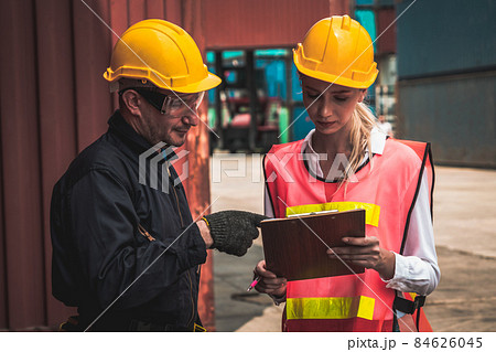Industrial worker works with co-worker at overseas shipping container yard Industrial worker works with co-worker at overseas shipping container yard 84626045