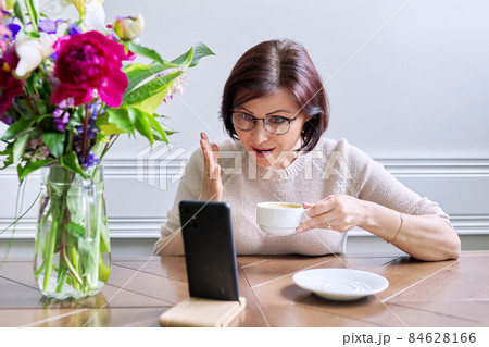 Middle-aged woman sitting at home using smartphone for video call 84628166