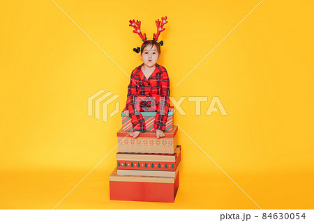Girl in red pajamas sitting on gift boxes against yellow background 84630054