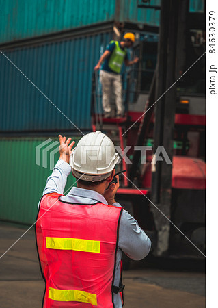 Industrial worker works with co-worker at overseas shipping container yard Industrial worker works with co-worker at overseas shipping container yard 84630379