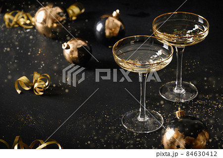 Festive New Year champagne flutes and Christmas gold baubles on black background. 84630412