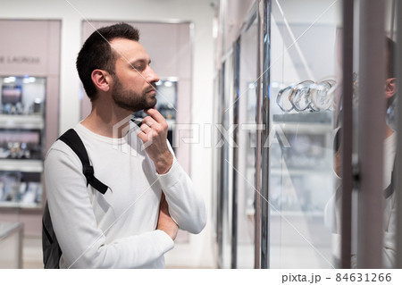 Photo of an adult handsome brunette man in a white sweatshirt and with a backpack chooses a stylish 84631266