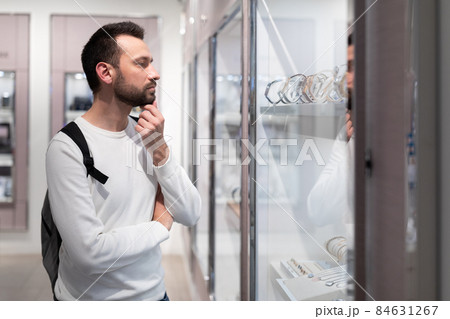 Photo of an adult handsome brunette man in a white sweatshirt and with a backpack chooses a stylish 84631267