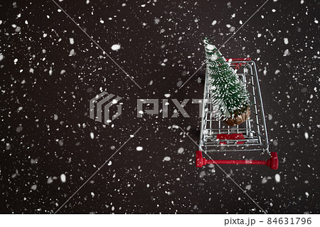Top view of a grocery cart with snowy Christmas trees on a dark snowy background with copy space for text. The apartment was lying. Winter, postcard template. 84631796