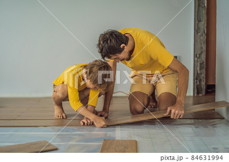 Father and son installing new wooden laminate flooring on a warm film floor. Infrared floor heating system under laminate floor 84631994