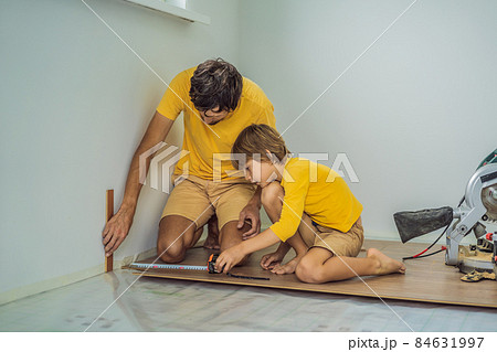 Father and son installing new wooden laminate flooring on a warm film floor. Infrared floor heating system under laminate floor 84631997
