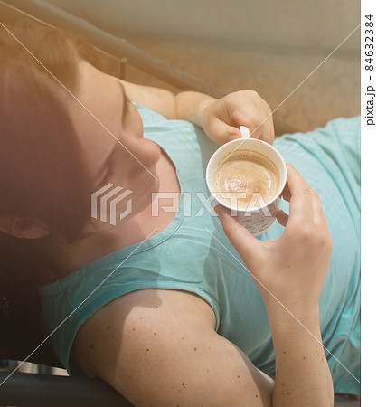 young caucasian happy woman drinking coffee in sunlight, top view young caucasian happy woman drinking coffee in sunlight, top view 84632384