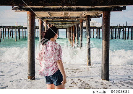 Turkey, Mediterranean Sea. Young woman turned away from the camera, running away from the waves under a wooden pier Turkey, Mediterranean Sea. Young woman turned away from the camera, running away from the waves under a wooden pier 84632385