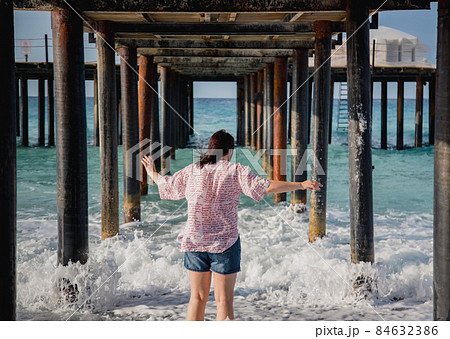 Turkey, Mediterranean Sea. Young woman turned away from the camera, running away from the waves under a wooden pier Turkey, Mediterranean Sea. Young woman turned away from the camera, running away from the waves under a wooden pier 84632386