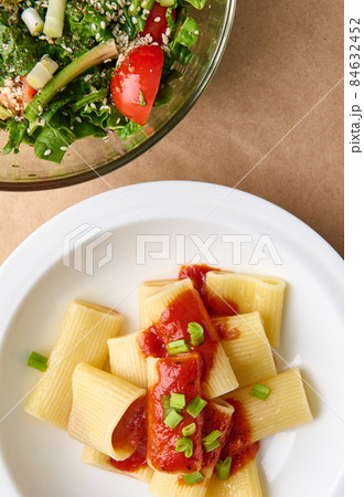 Flat lay. Cropped photo of a healthy vegan meal consisting of vegetarian herb salad and cooked italian pasta with tomato sauce and green onion garnish Flat lay. Cropped photo of a healthy vegan meal consisting of vegetarian herb salad and cooked italian pasta with tomato sauce and green onion garnish 84632452