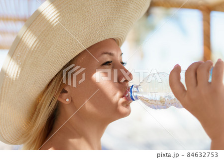 Beautiful woman in straw hat drinking pure water from bottle. Close-up view. 84632753