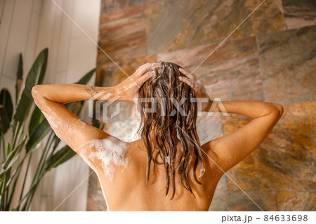 Back view of beautiful naked young woman taking shower in bathroom with marble tiles 84633698