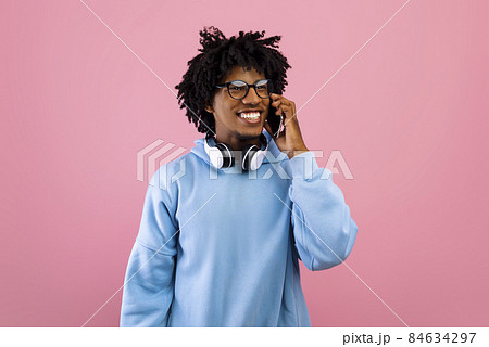 Happy black teenager with headphones talking on smartphone on pink studio background 84634297