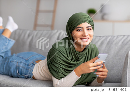 Arab woman in hijab lying on sofa, using mobile phone, checking social network, browsing web, communicating online Arab woman in hijab lying on sofa, using mobile phone, checking social network, browsing web, communicating online 84634401