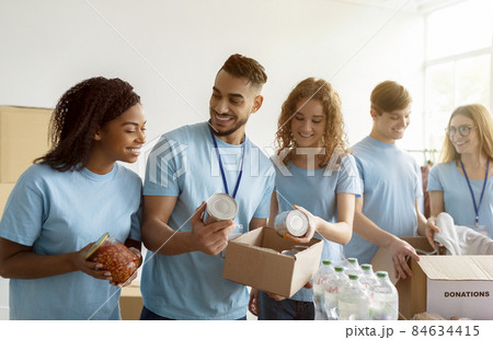 Humanitarian aid concept. Young diverse volunteers sorting and packing canned food in cardboard boxes, working together 84634415