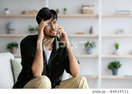 Upset indian guy having phone conversation, home interior Upset indian guy having phone conversation, home interior 84634511