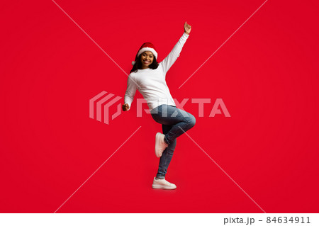 Attractive african american woman in Santa hat dancing on red Attractive african american woman in Santa hat dancing on red 84634911