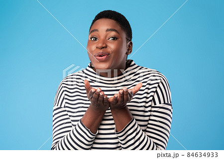 Cheerful Plus-Sized Black Woman Sending Air Kisses Over Blue Background 84634933