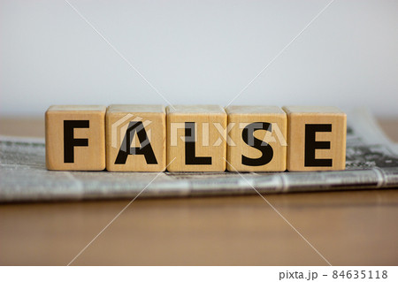 False in news symbol. Cubes placed on a newspaper form the word 'false'. Beautiful wooden table. White background. Business and false in news concept. Copy space. 84635118