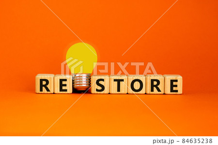 Restore symbol. Wooden cubes with the word 'restore'. Yellow light bulb. Beautiful orange background. Business and restore concept. Copy space. 84635238