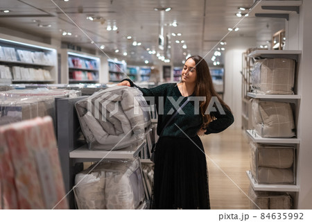 Woman with hand on waist examining folded blanket in bag while shopping in spacious modern mall 84635992