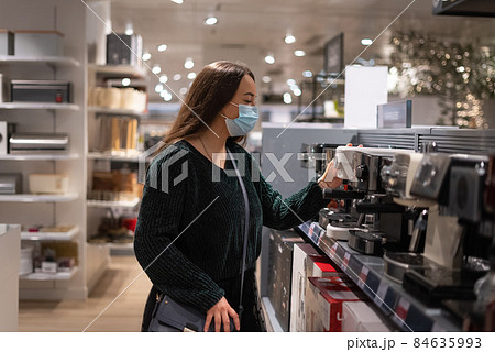 Woman in mask touching and examining coffee machine on shelf while shopping in contemporary mall Woman in mask touching and examining coffee machine on shelf while shopping in contemporary mall 84635993