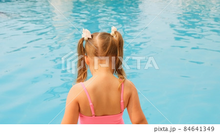 little girl 4-5 years old, dressed in a pink swimsuit, blowing soap balls in the pool on summer 84641349