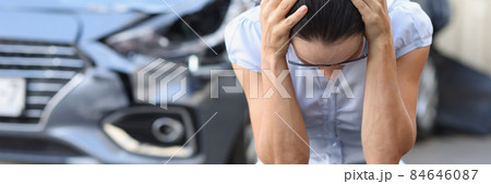 Frightened woman sits in front of wrecked car closeup Frightened woman sits in front of wrecked car closeup 84646087