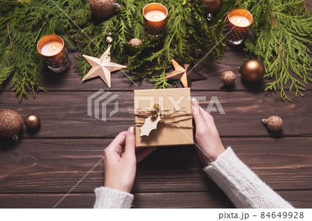 Woman holds gift box decorated with twine and a wooden tag. Christmas composition in brown. 84649928