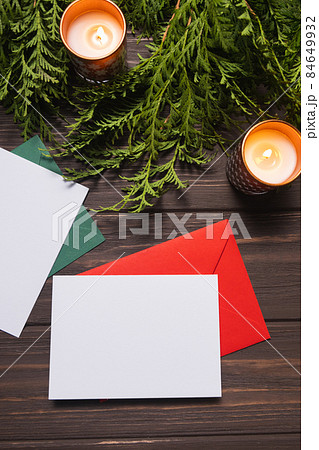 Christmas letters with greeting cards lie on a brown wooden table with fir branches and candles. 84649932