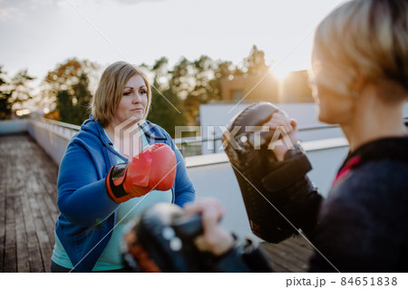 Overweight woman training boxing with personal trainer outdoors on terrace. Overweight woman training boxing with personal trainer outdoors on terrace. 84651838