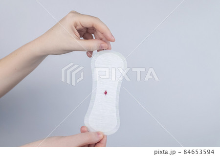 Hypomenorrhea. The woman shows a gynecological pad with a small drop of blood on it. Concept of small amounts during scanty menstruation. Complaints of pain and strange cycle. Diseases in gynecology Hypomenorrhea. The woman shows a gynecological pad with a small drop of blood on it. Concept of small amounts during scanty menstruation. Complaints of pain and strange cycle. Diseases in gynecology 84653594