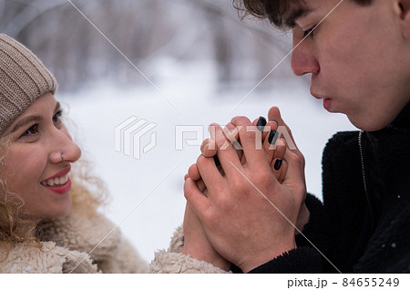 A young couple walks in the winter in the forest. The guy warms the girl's hands. 84655249