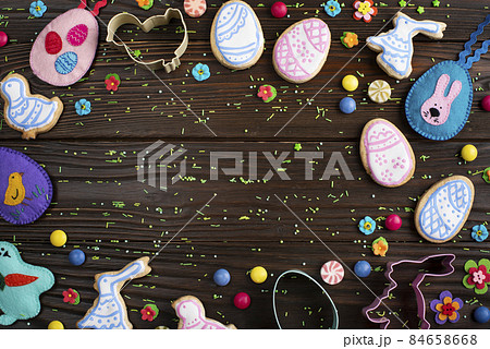 Cookie cutters, felt toys and Easter frosted cookies in shape of egg, chicken and rabbit on dark wooden background fat lay view. 84658668