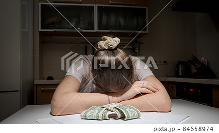 Stressed woman having to pay rent and bank loan lying on kitchen next to few money banknotes 84658974