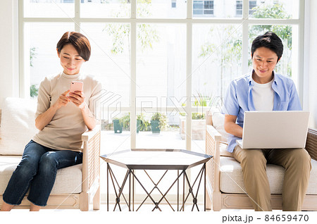 晴れの日の窓際でスマホとパソコンを見る夫婦 84659470