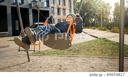 Happy smiling and laughing boy swinging on children playground at new courtyard. Concept of child development, sports and education. 84659827