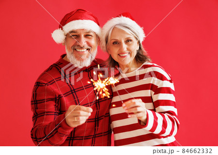 Happy overjoyed senior family couple in Santa hats with Bengal sparkler light celebrate New year 84662332