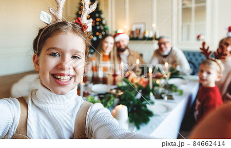 Happy little girl in reindeer antlers taking selfie of large family during Christmas celebration 84662414