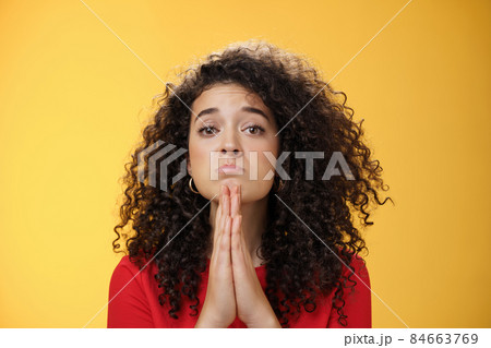 Please I beg you. Portrait of sad and cute curly-haired girl with angel eyes pouting holding hands in pray and looking hopeful at camera waiting for mercy asking apology, supplicating over yellow wall Please I beg you. Portrait of sad and cute curly-haired girl with angel eyes pouting holding hands in pray and looking hopeful at camera waiting for mercy asking apology, supplicating over yellow wall 84663769