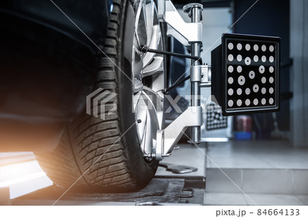 CLose-up car wheel indoors service maintenance repair center against laser sensor equipment diagnostics and 3d wheel alignment. Vehicle inside garage workshop for auto camber toe check fixing work CLose-up car wheel indoors service maintenance repair center against laser sensor equipment diagnostics and 3d wheel alignment. Vehicle inside garage workshop for auto camber toe check fixing work 84664133