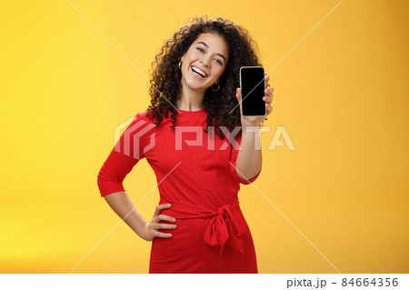 Carefree satisfied and happy attractive businesswoman presenting her best friend new mobile phone showing smartphone at camera laughing and smiling joyfully delighted with new purchase 84664356