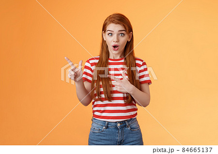 Wow awesome. Impressed excited beautiful redhead woman look astonished explain amazing news, stare camera thrilled talking about advertisement, pointing left upbeat impressed, orange background 84665137